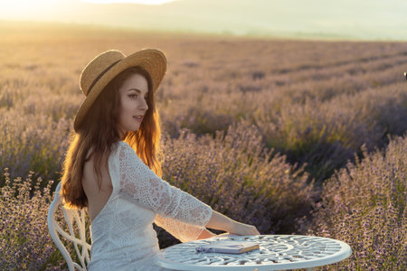 A woman wearing a straw hat is sitting in a field. She is smiling and she is enjoying the moment.の写真素材