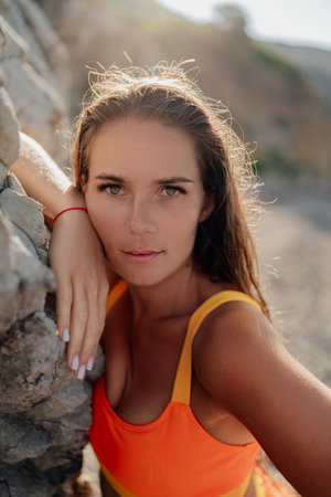 A woman in an orange tank top is leaning against a rockの写真素材