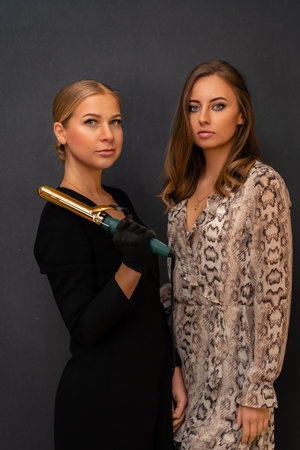 Two women are posing for a photo, one holding a hair curler. Scene is casual and friendly, as the women are smiling and looking at the camera.の写真素材