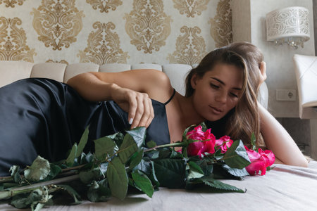 A woman is laying on a bed with a bouquet of red roses in her lap. Concept of romance and intimacy, as the woman is surrounded by the flowers and he is in a relaxed and comfortable position.の写真素材