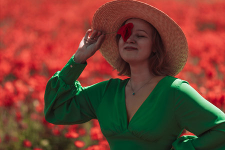 A woman in a green dress is standing in a field of red flowersの写真素材