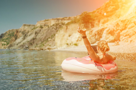 Woman laptop sea. Freelancer woman in sunglases floating on an inflatable big pink donut with a laptop in the sea. People summer vacation rest lifestyle conceptの写真素材