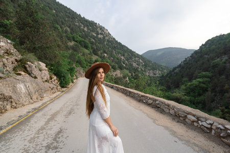 A woman in a white dress is standing on a road with a brown hat onの写真素材