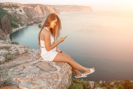 Happy woman in white shorts and T-shirt, with long hair, talking on the phone while enjoying the scenic view of the sea in the background.の写真素材