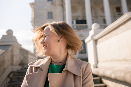 A woman with long hair is standing on a set of stairs. She is wearing a green shirt and a tan coat.の写真素材