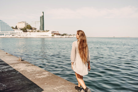 woman in a white dress is walking on a pier near the water. The scene is peaceful and serene, with the womans long hair blowing in the wind.の写真素材