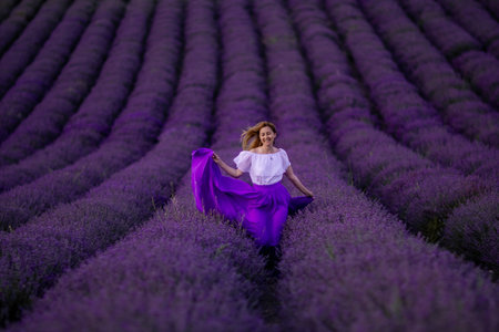 Lavender Field Woman Purple Skirt - A young woman wearing a purple skirt dances in a field of blooming lavender flowers during a summer day. The photo was taken from a high angle, showcasing the vastness of the field and the beauty of the lavender. The womans joyful expression adds a sense of life and vibrancy to the image.の写真素材