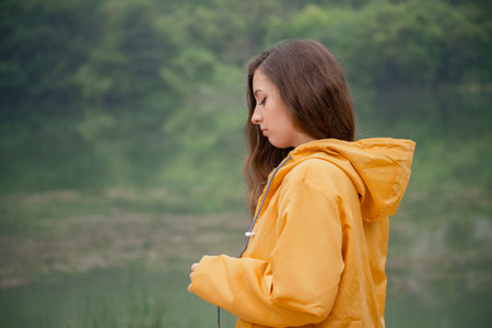A woman in a yellow jacket is standing by a lakeの写真素材