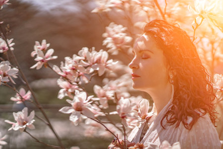 Magnolia park woman. Stylish woman in a hat stands near the magnolia bush in the park. Dressed in white corset pants and posing for the camera.の写真素材
