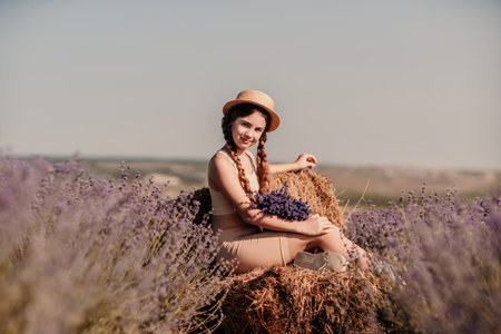 girl sitting field lavender and wearing a straw hat. She is smiling and holding a bouquet of flowersの写真素材