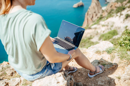A woman is sitting on a rock with a laptop open in front of herの写真素材
