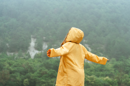 A woman in a yellow raincoat is standing in the rain and looking up at the skyの写真素材