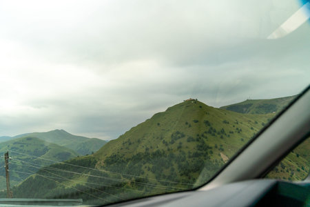 A car window shows a mountain range with a cloudy sky