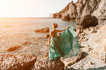 Woman green dress sea. Woman in a long mint dress posing on a beach with rocks on sunny day. Girl on the nature on blue sky background.の写真素材