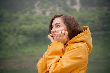 A woman in a yellow raincoat is looking up at the skyの写真素材