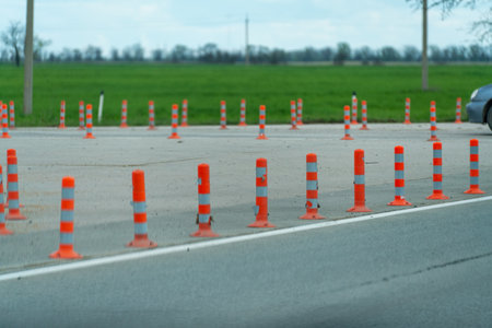 A row of orange and white traffic cones are lined up on a road. The scene is quiet and peaceful, with no cars or people in the area.の写真素材