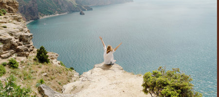 A woman is sitting on a rock overlooking the ocean. She is smiling and she is enjoying the view.の写真素材