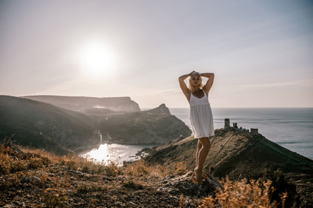 A blonde woman stands on a hill overlooking the ocean. She is wearing a white dress and she is enjoying the view.の写真素材
