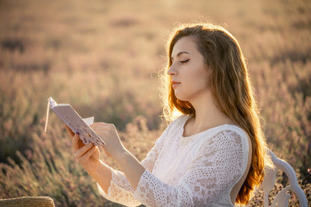 A woman is sitting in a field reading a bookの写真素材