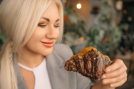 A blonde woman is eating a chocolate pastry. She is smiling and she is enjoying her treat.の写真素材