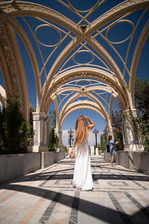 Woman, White Dress, Archway - A woman in a white dress walks through an ornate archway with a blue sky above.の写真素材