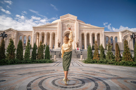 A woman in a long skirt and sweater poses in front of a large, ornate building with columnsの写真素材