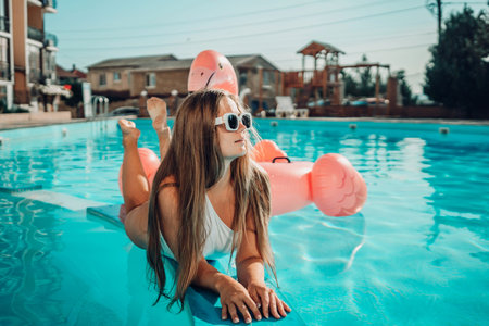 A woman is laying on a pool float in a pool. The pool is blue and the woman is wearing a white...