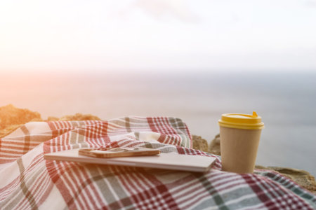 Laptop coffee on blanket with ocean view. Illustrating serene outdoor laptop use. Freelancer...