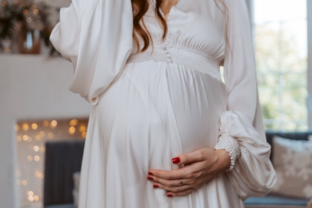 A pregnant woman is wearing a white dress and holding her stomach. Concept of anticipation and excitement for the upcoming arrival of the baby.の写真素材