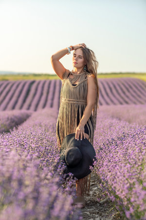 A woman is standing in a field of purple flowers, wearing a black dress and a black hat.の写真素材