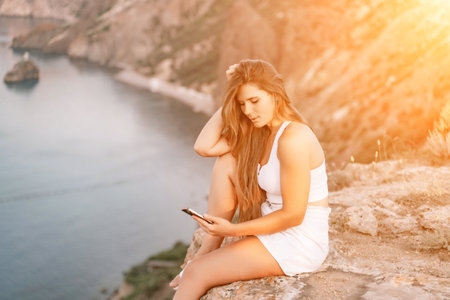 Happy woman in white shorts and T-shirt, with long hair, talking on the phone while enjoying the scenic view of the sea in the background.の写真素材