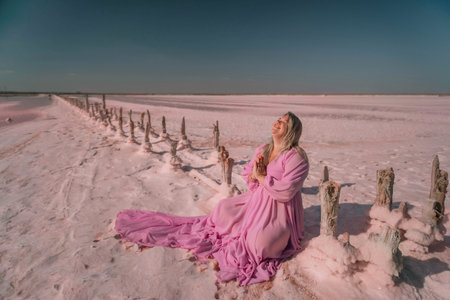 A woman in a pink dress sits on a fence in a pink lake.の写真素材