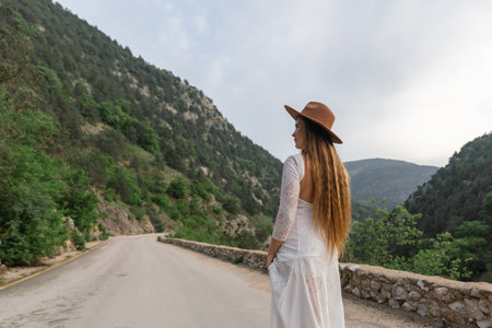 A woman in a white dress is standing on a road, looking out at the mountainsの写真素材