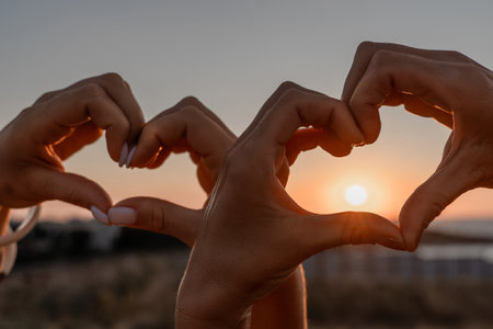 Hands Heart Sunset - Two hands forming a heart shape against the setting sun, symbolizing love and affection.の写真素材