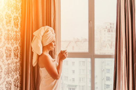 Young serene relaxed woman in spa bath towel drinking hot beverage tea coffee after taking shower bath at home. Beauty treatment, hydration concept.の写真素材