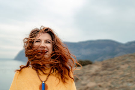 Portrait windswept hair happy woman against a backdrop of mountains and sea. Daylight illuminates the tranquil outdoor settingの写真素材