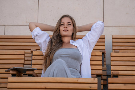 Woman, Bench, Relaxation - A woman relaxes on a bench outdoors, leaning back with her hands behind her head.の写真素材