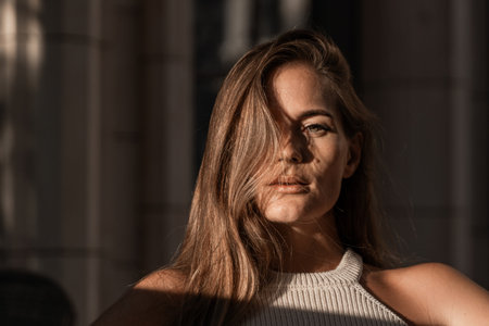 Woman Portrait Sunlight Closeup - A woman with long brown hair sits in the sunlight with her face partially obscured by her hair.の写真素材
