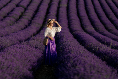 A woman stands in a field of purple flowers, wearing a straw hatの写真素材