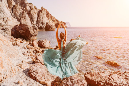 Woman green dress sea. Woman in a long mint dress posing on a beach with rocks on sunny day. Girl on the nature on blue sky background.の写真素材