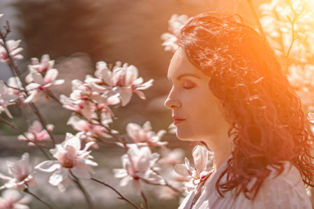 Magnolia park woman. Stylish woman in a hat stands near the magnolia bush in the park. Dressed in white corset pants and posing for the camera.の写真素材