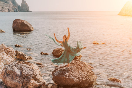 Woman green dress sea. Woman in a long mint dress posing on a beach with rocks on sunny day. Girl on the nature on blue sky background.の写真素材