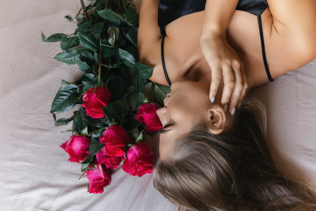 A woman is laying on a bed with a bouquet of red roses next to her. Concept of romance and intimacy, as the woman is surrounded by the flowers and he is in a relaxed and comfortable position.の写真素材