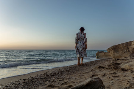Woman Beach Sunset - A lone woman stands on a sandy beach at sunset, gazing out at the ocean.の写真素材