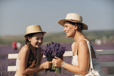 A woman and a child are sitting on a bench in a field of purple flowers lavande. The woman is holding a bouquet of flowers and the child is holding a bouquet of flowers as wellの写真素材