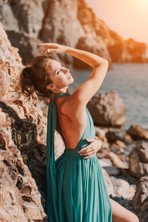 Woman green dress sea. Woman in a long mint dress posing on a beach with rocks on sunny day. Girl on the nature on blue sky background.の写真素材