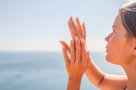 A woman is wearing a lot of rings on her hands and is looking out at the oceanの写真素材