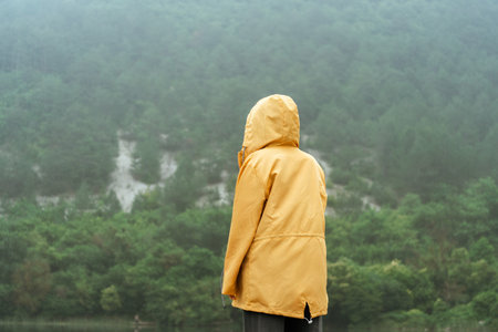 A person is standing in the woods wearing a yellow jacket
