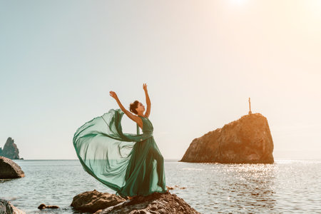 Woman green dress sea. Woman in a long mint dress posing on a beach with rocks on sunny day. Girl on the nature on blue sky background.の写真素材