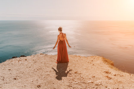 Woman red dress sea. Female dancer in a long red dress posing on a beach with rocks on sunny day. Girl on the nature on blue sky background.の写真素材